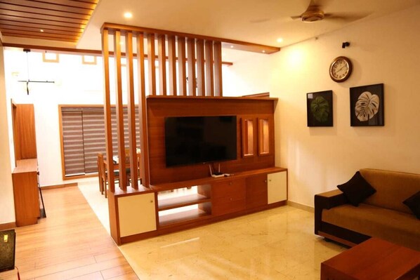 A modern living room with a flat-screen TV, wooden entertainment unit, and a sofa.