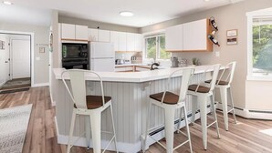 A modern kitchen with a central island, bar stools, and a view of the outdoors.