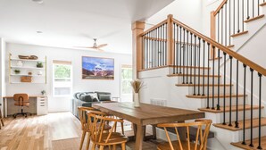 A spacious living area with a wooden dining table, chairs, and a staircase with wooden railings.