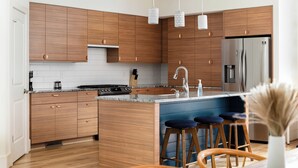 A modern kitchen with wooden cabinets, a stainless steel refrigerator, and a central island with bar stools.