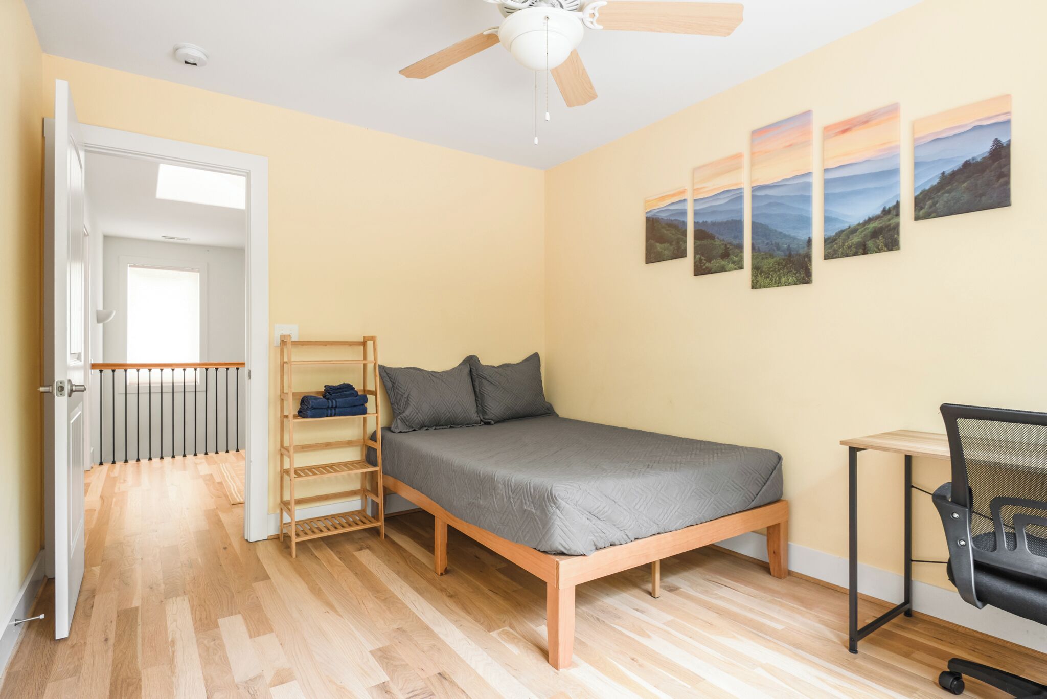 Un dormitorio con cama, escritorio, silla, ventilador de techo y una puerta que da a otra habitación.