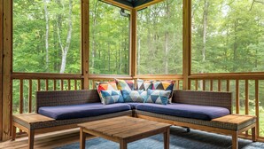 A covered deck with a wooden bench and a sofa with colorful cushions.