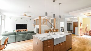 A modern kitchen with a central island, wooden flooring, and a staircase leading to an upper level.
