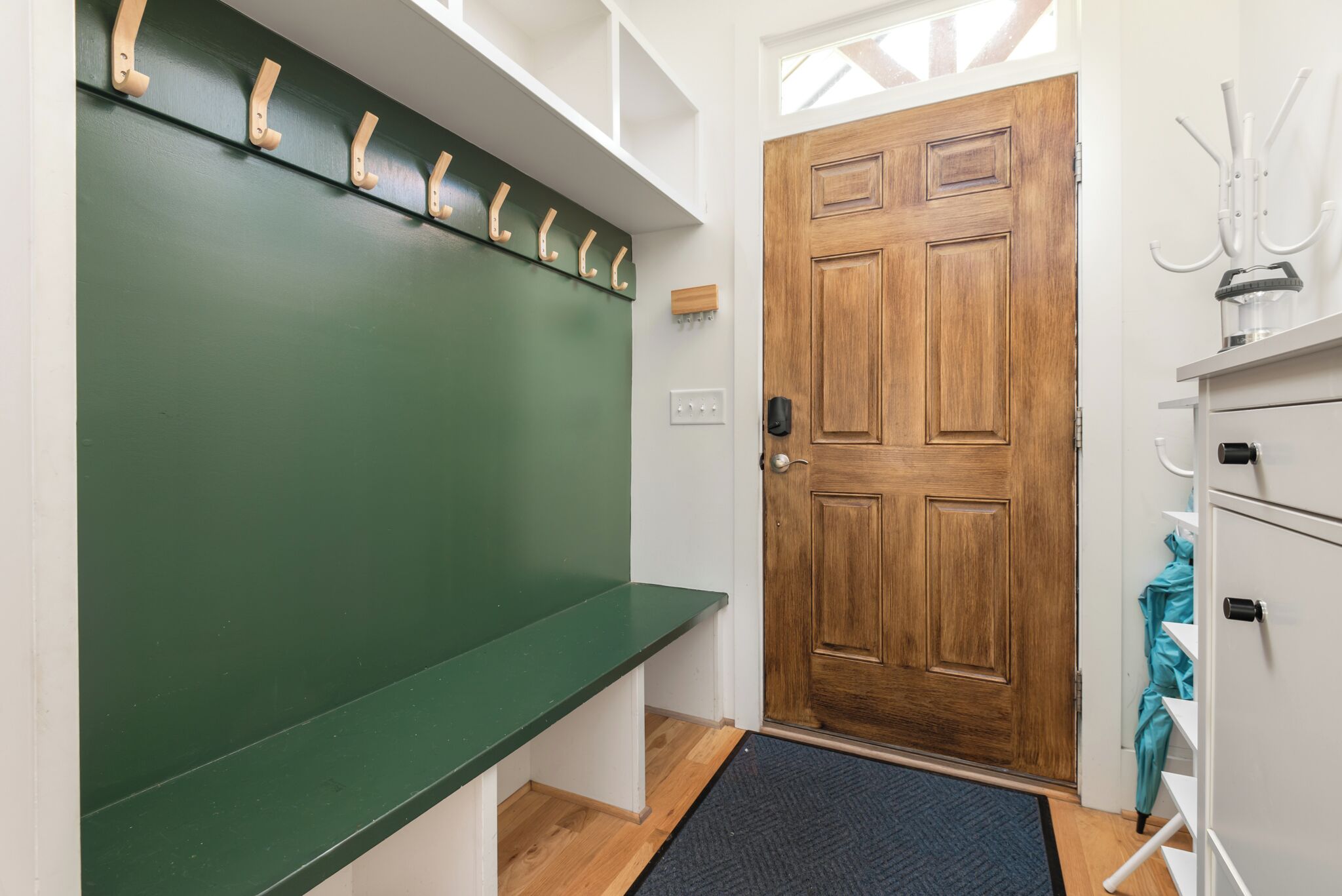 Un pasillo con un banco verde, una puerta de madera y un perchero.
