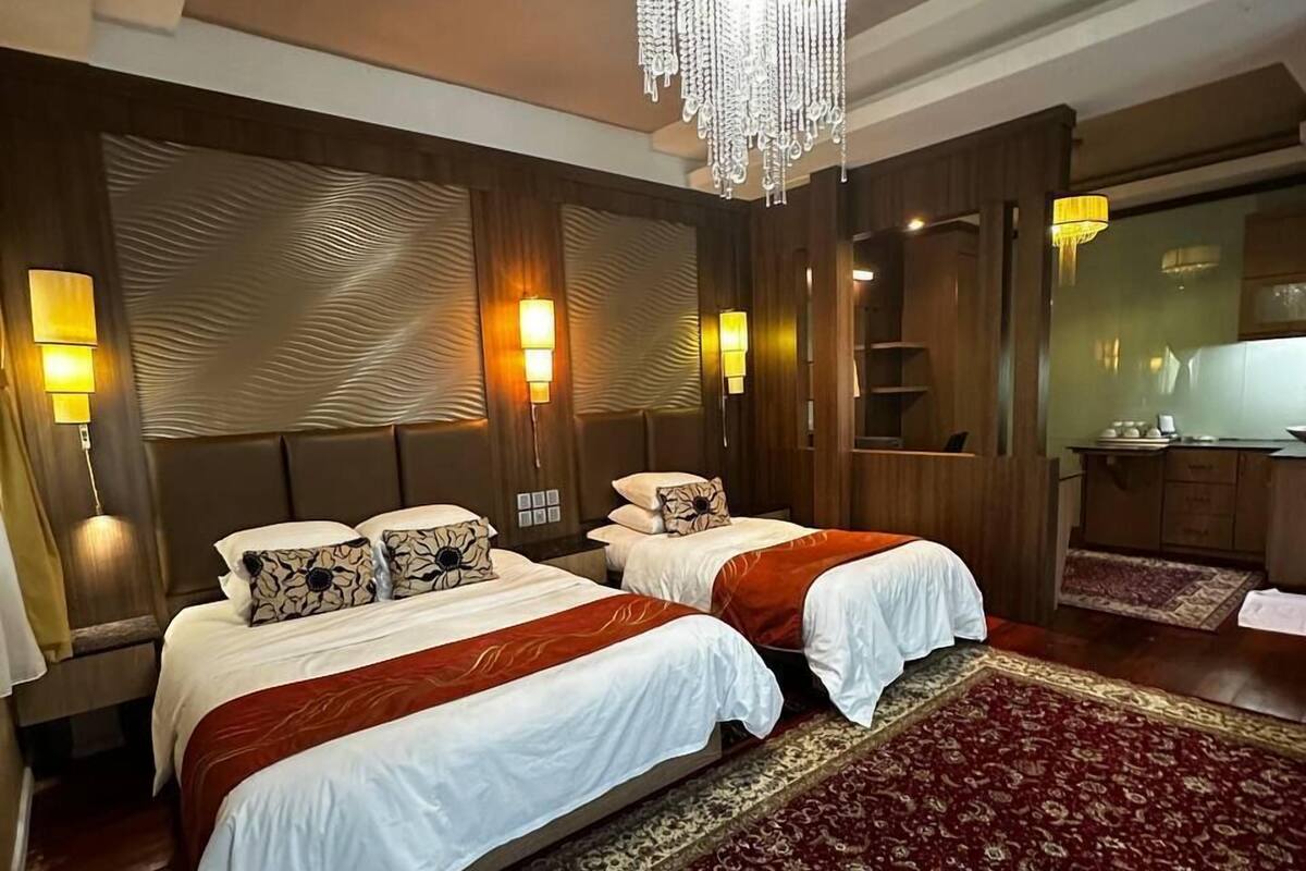 Ein Hotelzimmer mit zwei Betten, einer Kristallleuchter, Wandleuchten und einem gemusterten Teppich.