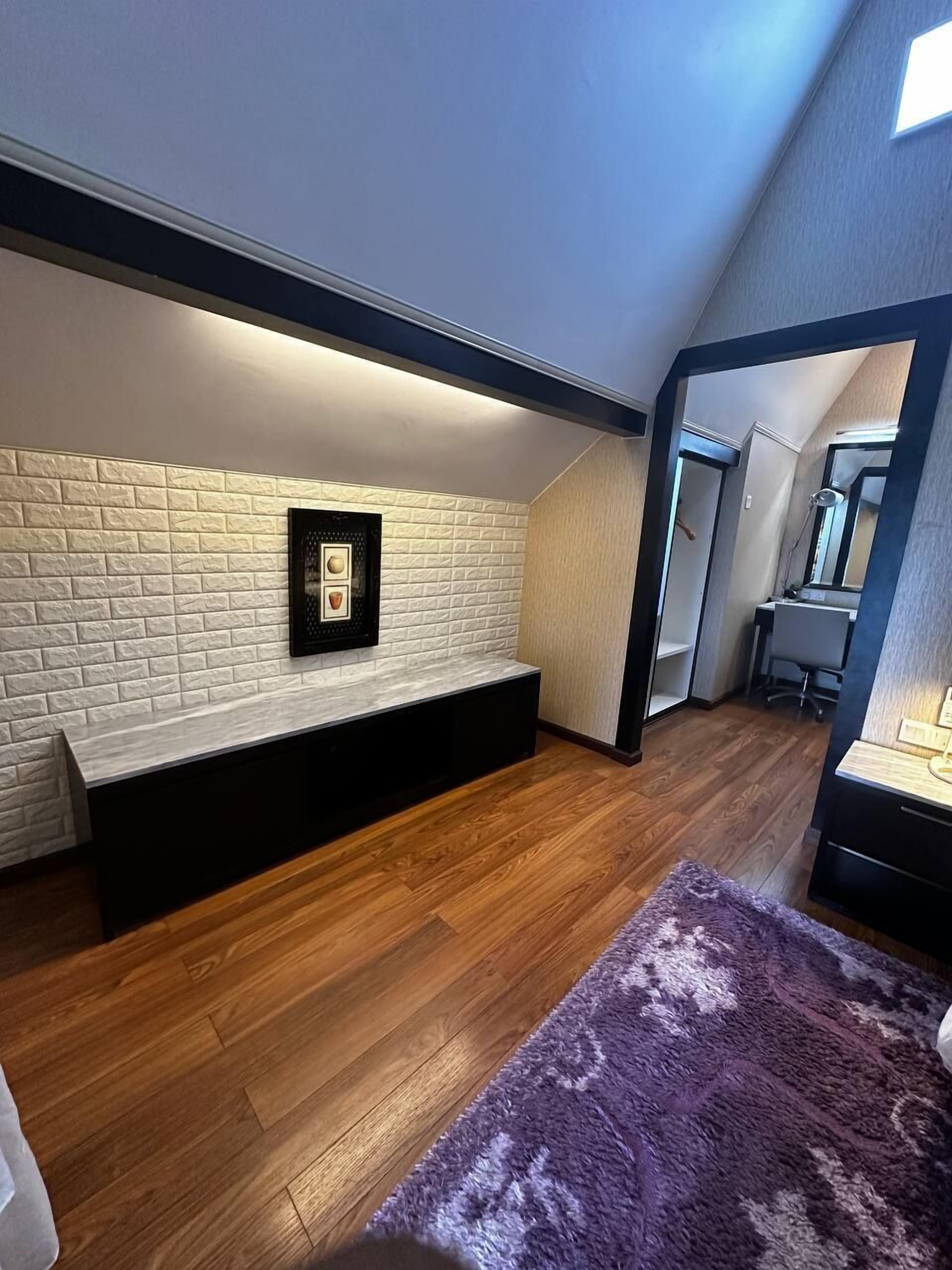 Een slaapkamer met zolderafwerking, houten vloer, een witte baksteenmuur, een zwarte bank en een paars tapijt.