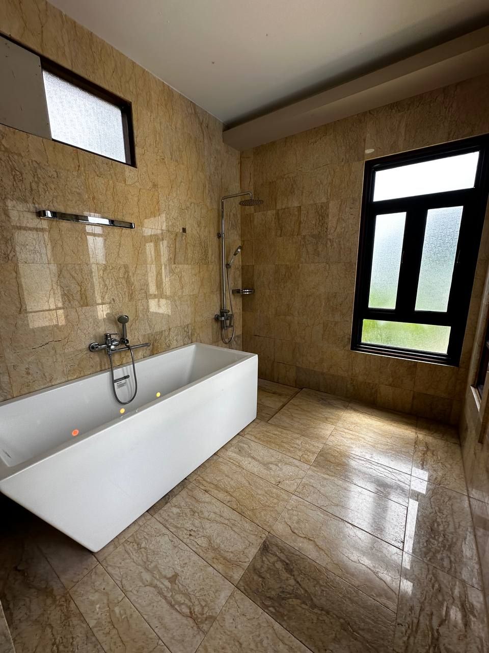 Een moderne badkamer met een groot bad, een douche en een raam voor natuurlijk licht.