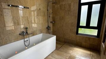 Een moderne badkamer met een groot bad, een douche en een raam voor natuurlijk licht.