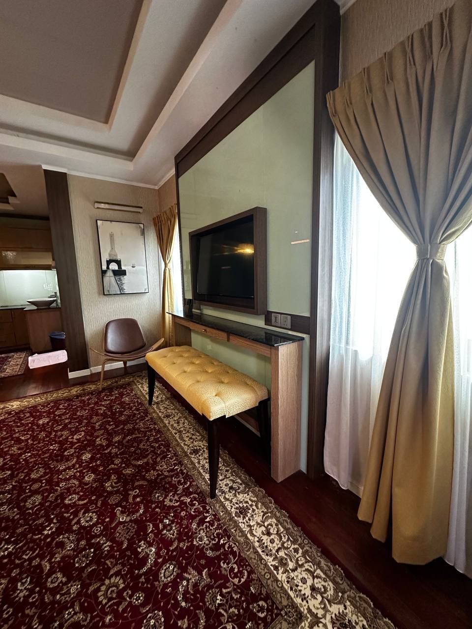 A hotel room with a large bed, a TV, a bench, and a view of the city skyline.