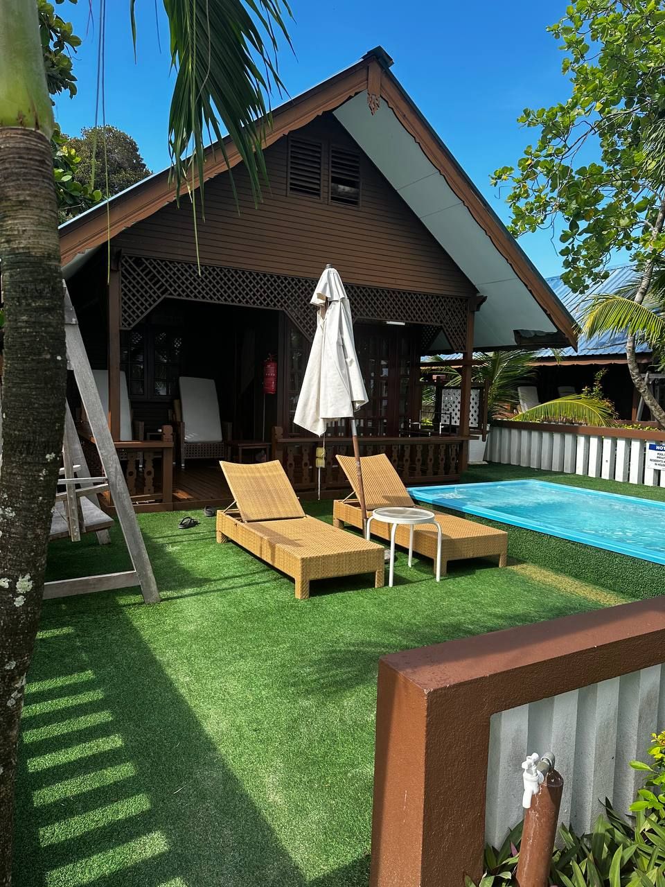 A poolside area with two lounge chairs and a table, a covered seating area, and a swimming pool.