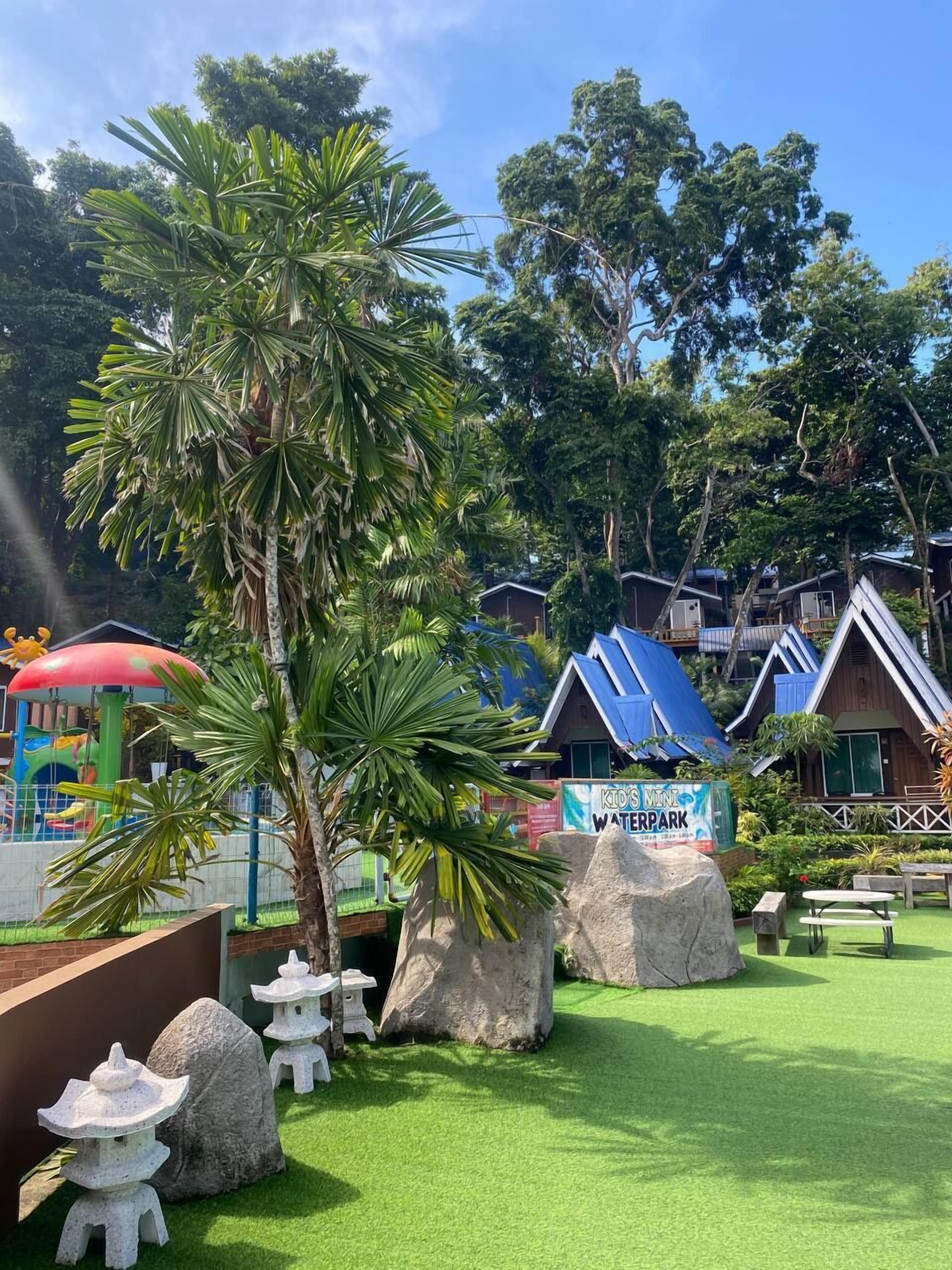 A waterpark area with a sign for 'Kids Mint Waterpark', surrounded by palm trees and rocks.