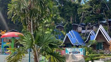Un espace aquatique avec un panneau indiquant « Kids Mint Waterpark », entouré de palmiers et de rochers.