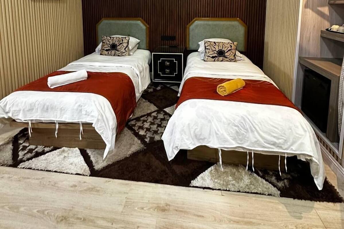 Ein Hotelzimmer mit zwei Betten, einem Deckenventilator, einer fest installierten Klimaanlage und einem kleinen Tisch mit Lampe.