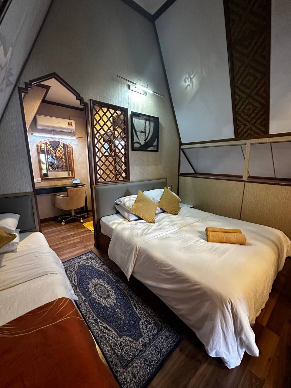 A bedroom with a bed, a desk, and a chair. There is a window with a wooden lattice, a wall-mounted air conditioner, and a framed picture.