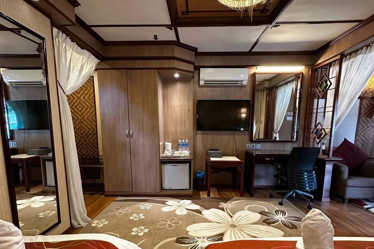Ein Hotelzimmer mit zwei Betten, einem großen Spiegel, einem Fernseher und einer Kristallleuchtre.