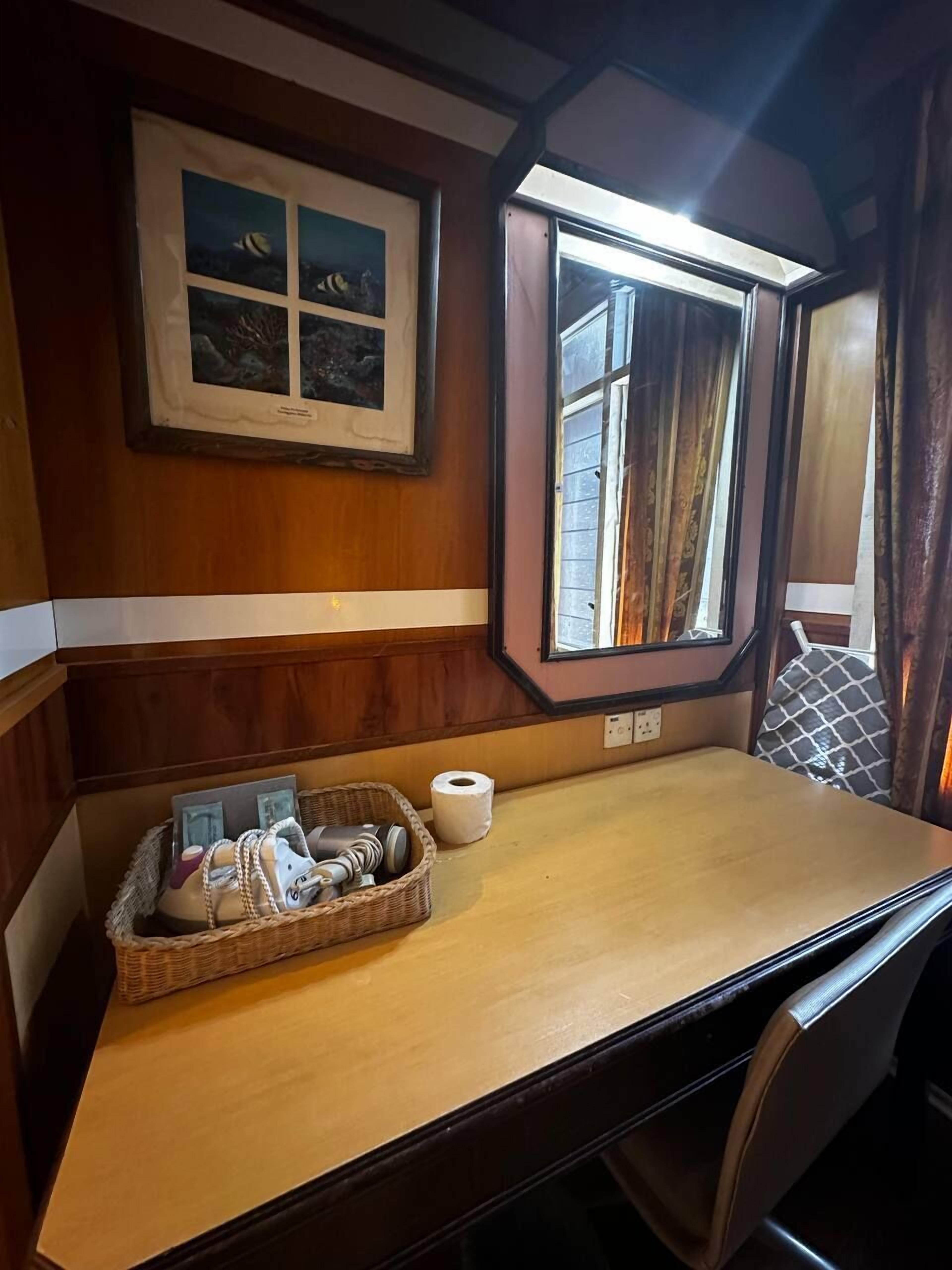 Interior de madera con una ventana, un cuadro enmarco, una mesa y una cesta con objetos.