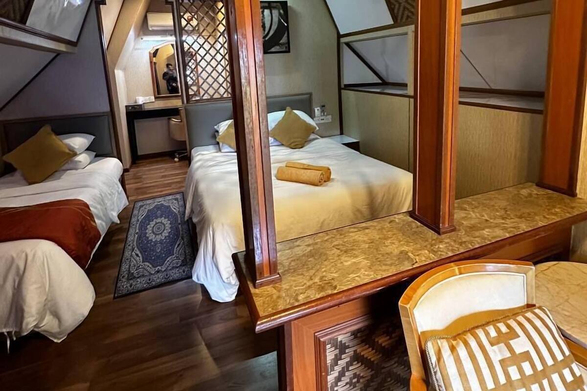 Ein schrägwandiges Schlafzimmer im Dachgeschoss mit Holzbalken, zwei Betten, einem Nachttisch und einem gemusterten Teppich.