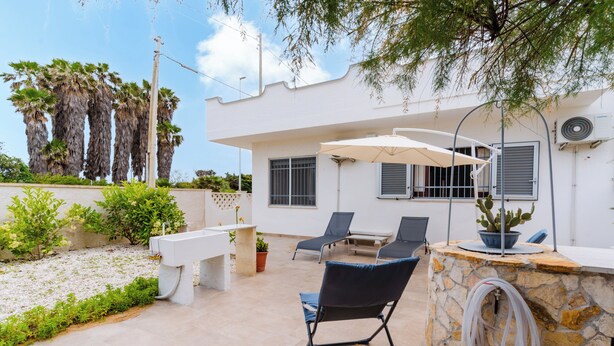 A patio with a stone wall, a white bench, and a table with chairs. - Alba Salentina by BarbarHouse (Torre Rinalda)