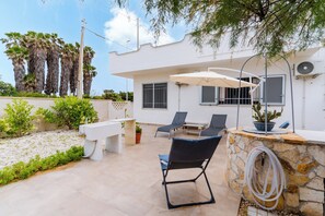 A patio with a stone wall, a white bench, and a table with chairs.