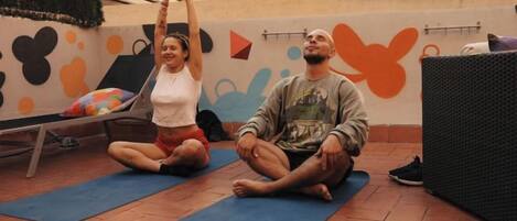 Two people sitting on yoga mats in an outdoor area with a wall featuring abstract designs.
