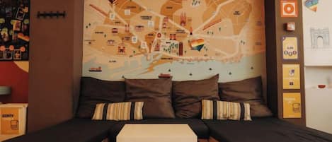 Una habitación con un gran mapa de Barcelona, dos camas, una mesita pequeña y una pared con varias decoraciones.
