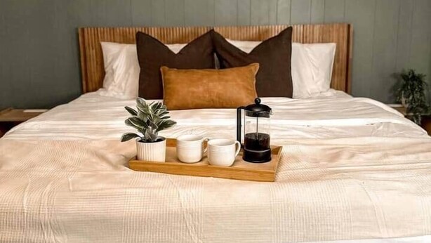 Een netjes opgemaakt bed met een dienblad, een nachtkastje met een lamp en wandplanken met decoratieve objecten.