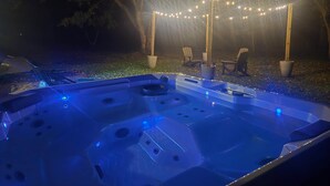 Een bubbelbad met blauwe verlichting, omringd door bomen en lichtjes.
