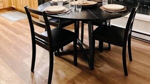 Een eethoek met een ronde tafel, zwarte stoelen en een vaas met gedroogde planten.