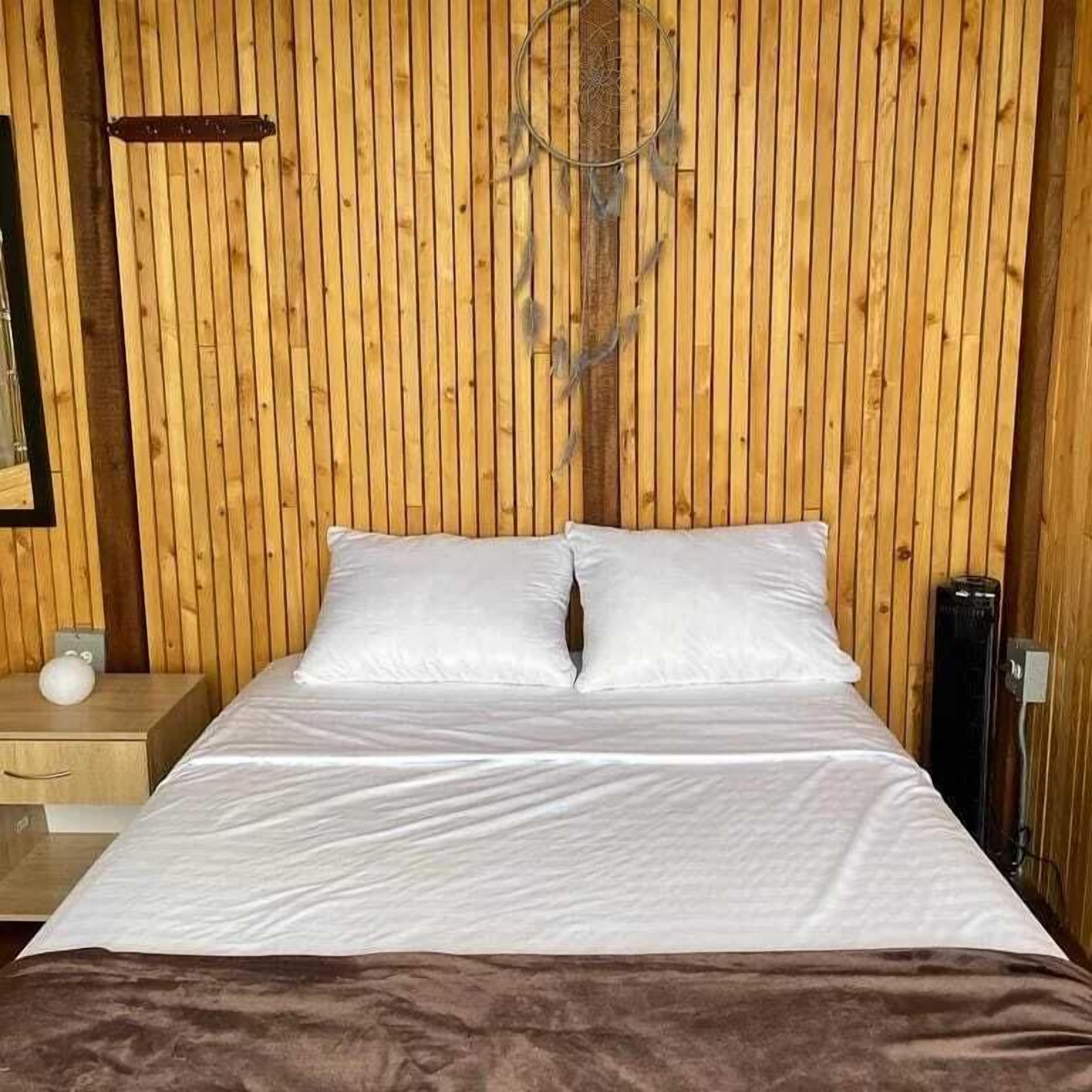 A wooden-paneled room with a bed, a nightstand, and a wall-mounted dreamcatcher.