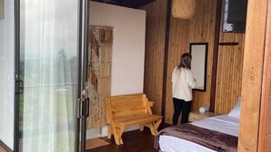 A bedroom with a bed, a bench, a wall-mounted TV, and a sliding glass door leading outside. - Samadhi Glamping (El Penol)