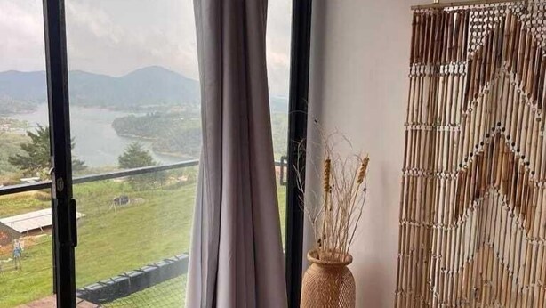 A room with a large window, a bamboo wall decor, and a wicker vase. - Samadhi Glamping (El Penol)