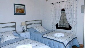 Una camera da letto con due letti, un comodino con una lampada, una finestra con tende e un quadro appeso al muro.