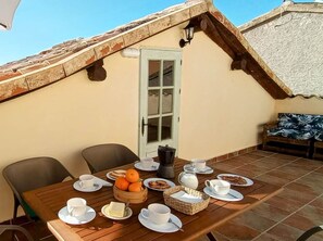 A dining area with a table set for breakfast, including plates, cups, and a basket of oranges.