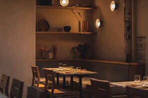 Un comedor tenuemente iluminado con una mesa preparada para dos personas, rodeada de sillas.