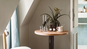 Una mesa redonda de madera con una planta en maceta, una jarrón blanco y vasos de cristal.