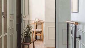Un pasillo con una silla de madera, una mesita con una planta y una puerta con picaporte negro.
