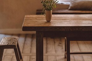 A wooden table with a potted plant, a wooden stool, and a patterned rug on a wooden floor.