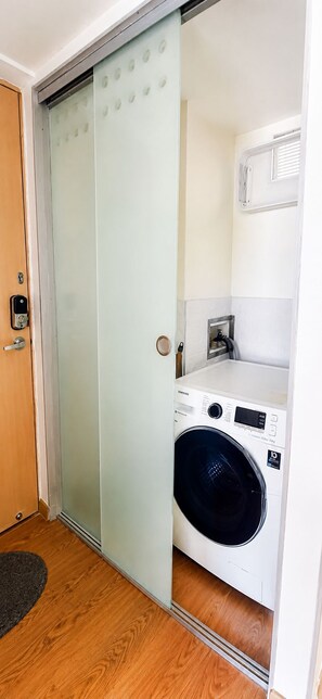 A room with a wooden floor, a white washing machine, and a sliding door with frosted glass panels. - Luxury Laureles LA 70-Medellin Stunner (Medellín)