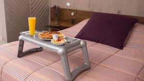 A bed with a striped bedspread, a purple pillow, and a breakfast tray with toast, fruit, and orange juice.