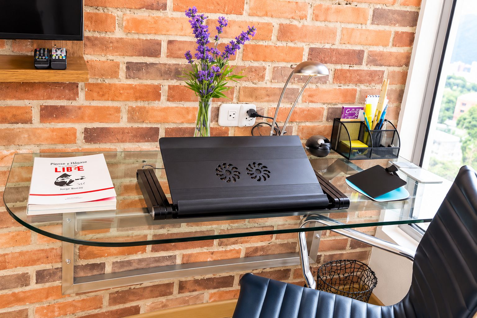 Un espacio de trabajo moderno con una computadora portátil, un libro, un florero con flores y una lámpara de escritorio.