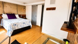 Quarto moderno com cama, cabeceira de madeira e mesa de vidro.