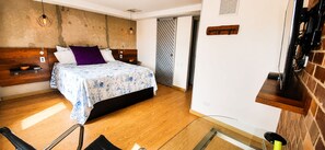 Quarto moderno com cama, cabeceira de madeira e mesa de vidro.