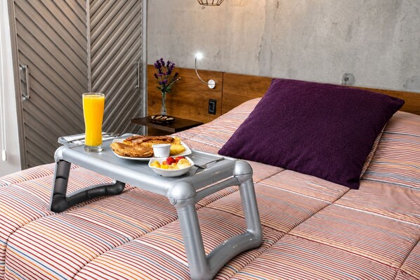 A bed with a striped blanket, a purple pillow, and a bedside table with breakfast items including toast, eggs, and a glass of orange juice.