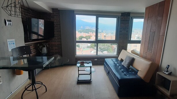 A modern living room with a glass table, a black sofa, and a large window offering a city view.