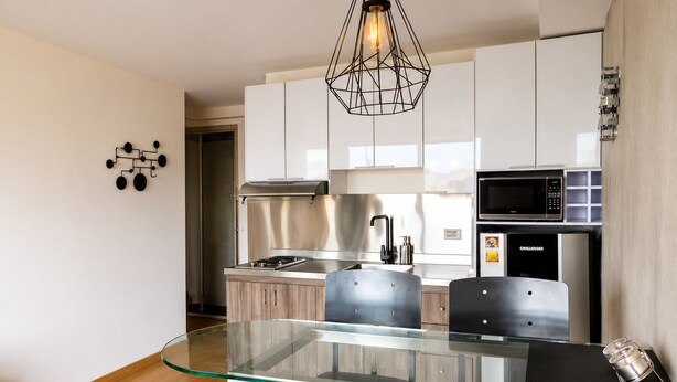 Cozinha moderna com mesa de jantar de vidro, eletrodomésticos de aço inoxidável e luminária geométrica.