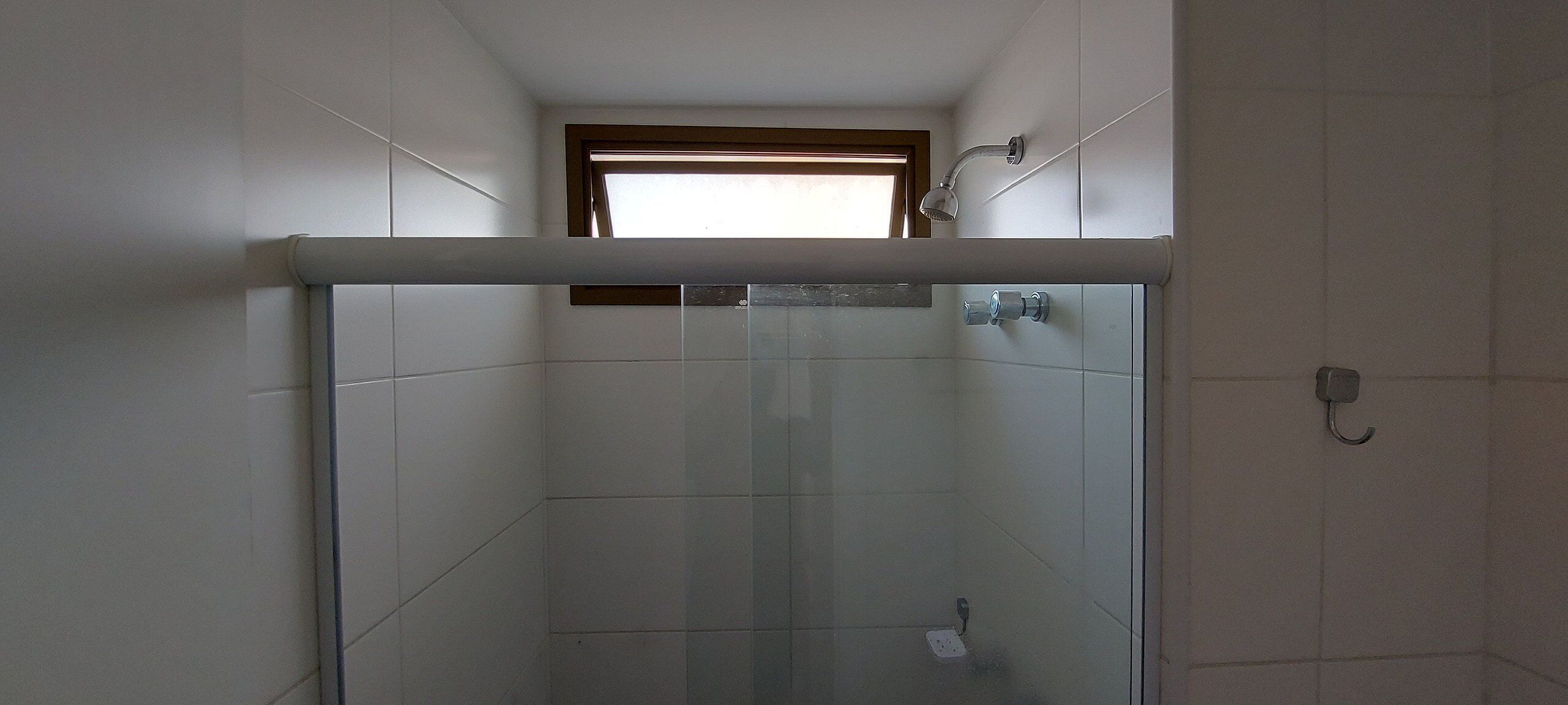 A glass-enclosed shower with a window above, white tiled walls, and a visible electrical outlet.