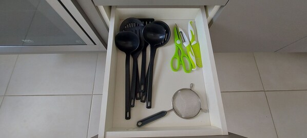 Un cajón con utensilios de cocina, como espátulas, un colador y tijeras.