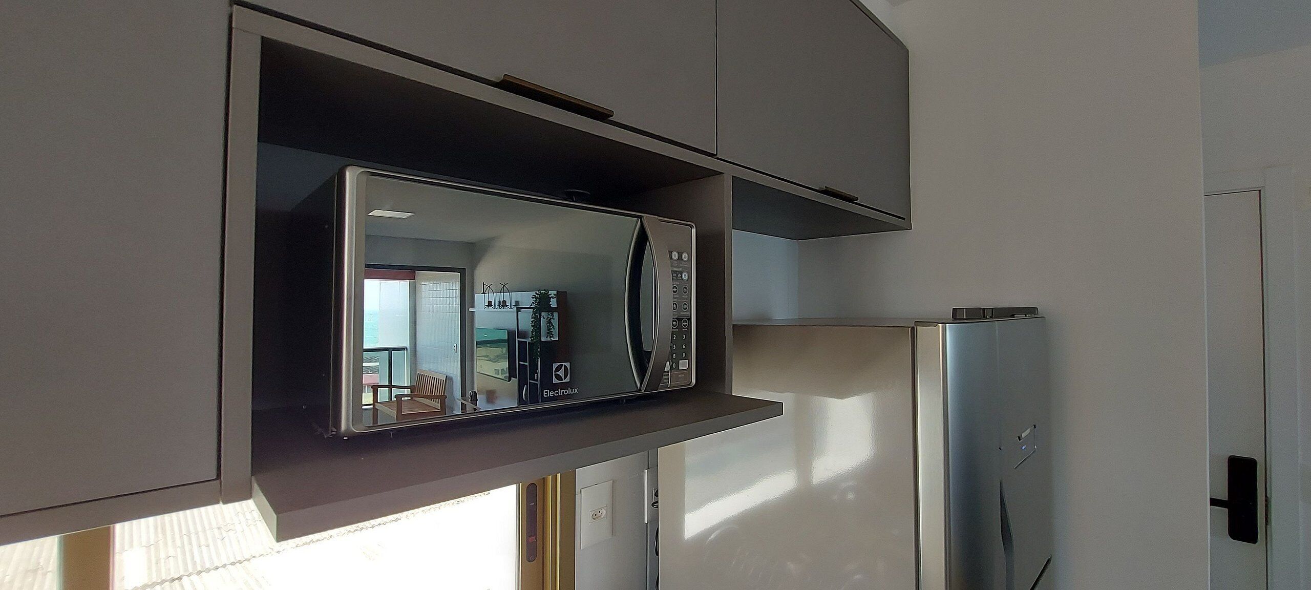 A compact kitchen with a built-in microwave, a refrigerator, and a window providing natural light.