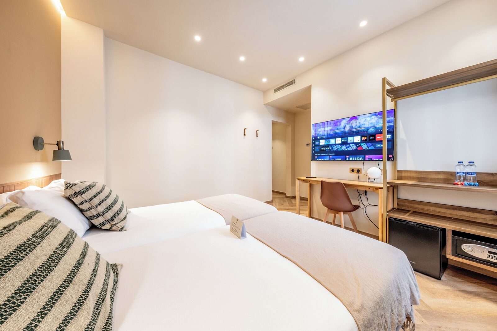 A hotel room with a large bed, a desk with a computer, and a TV on the wall.