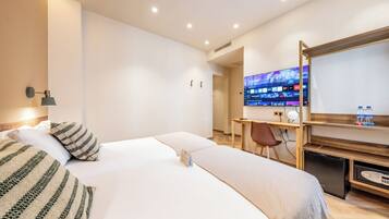 A hotel room with a large bed, a desk with a computer, and a TV on the wall.